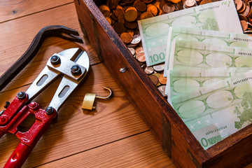 Geldscheine und Münzen liegen in einer aufgebrochenen Geldtruhe