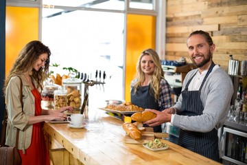 Woman using laptop and waiter cutting bread at counter