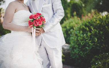 Bride holds a wedding red rose bouquet in hands, the groom hugs