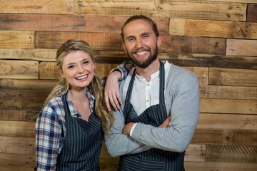 Smiling waiter and waitress standing against wooden wall in cafe