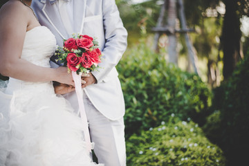 Bride holds a wedding red rose bouquet in hands, the groom hugs