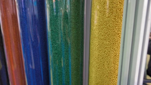 Samples of multi-colored plastic pellets in transparent containers. In the tubes are blue, white, green, red, yellow, pink, grey polymer granules. Shot in motion