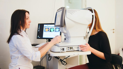 Modern ophthalmologist examining attractive woman's eyes with modern hi-tech equipment - obrazy, fototapety, plakaty