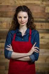 Portrait of waitress standing with arms crossed against wooden wall