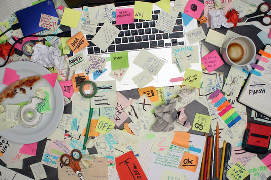 Top view on office desk with laptop computer and post it notes all around. Overwhelmed with work concept.
