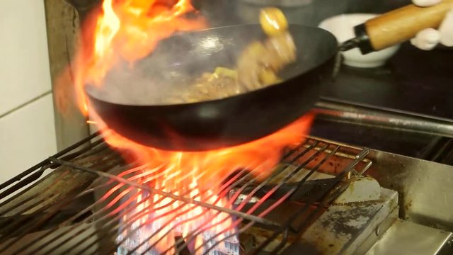 Asian restaurant, chinese chef cooking food with red meat beef and vegetables in wok pan on fire. Stir fry pan with flames. Slow motion.