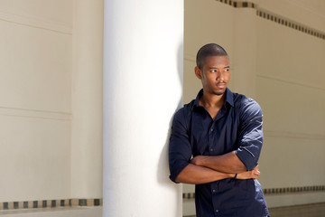 serious young black man leaning against wall with arms crossed