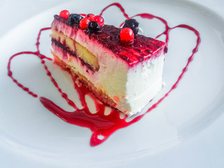 Close up of a slice of berries mousse cake with white cream. Puff pastry, fruits and cream with decorative strawberry jam. Flat lay aerial view. Local italian food.
