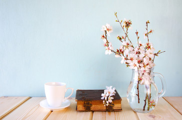old book, cup of coffee next to spring white flowers