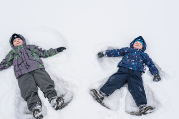 Fototapeta na wymiar Two little siblings kid boys in colorful winter clothes making snow angel, laying down on . Active outdoors leisure with children in . Happy brothers