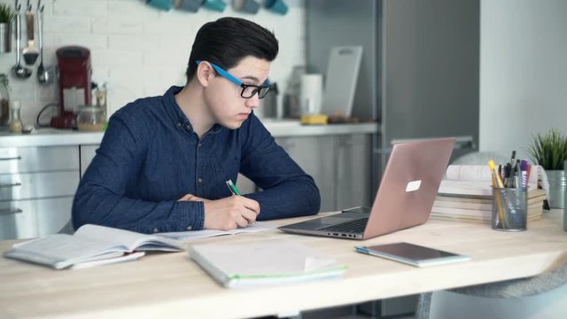Young tired, overworked teenager doing homework with laptop computer at home

