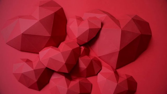Heap of red polygonal paper heart shapes on red background, top view, rotating video