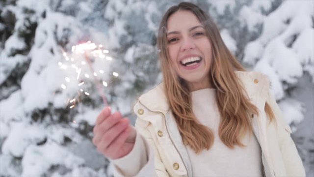 Young positive girl in winter forest snowy. Christmas and sparklers