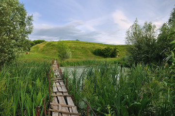 A broken wooden bridge through the reeds to the green hills