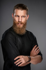 Portrait of serious hipster man with beard and mustashes standing with folded hands looking to the side