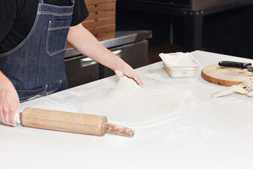 Fototapeta na wymiar Roll out the dough. Closeup hand of chef baker in uniform blue apron cook pizza at kitchen