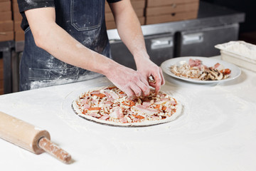 Cooking pizza. arranges meat ingredients on the dough preform. Closeup hand of chef baker in uniform blue apron cook at kitchen