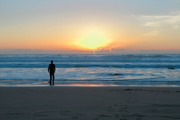 The groom in a suit on the ocean at sunset