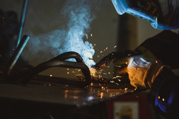 Welder working on a piece of steel pipe, sparks and smoke