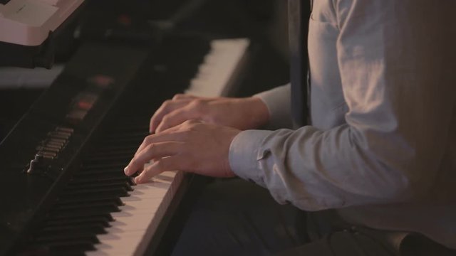 Musician playing at electronic piano. Musician dressed up in shirt and tie playing rhythmic music at synthesizer.