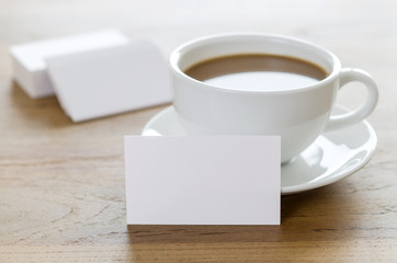 Blank business cards and cup of coffee on wooden table.