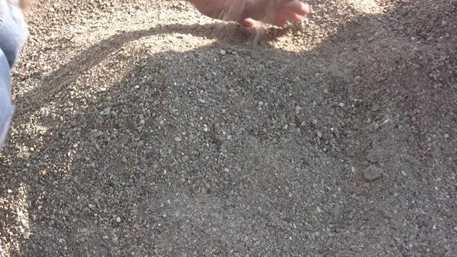 Two kids playing in a gravel pit of dusty sand.  Sand is pouring through their hands.

