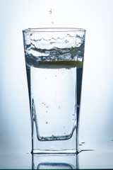 Glass glass of water with lemon on the isolated background. Mountain mineral pure mountain water with gas bubbles and a lemon slice and spray tonic refreshing sports drink.