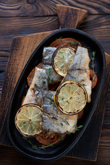 Baked sea bass slices with tomatoes and lemon in a frying pan
