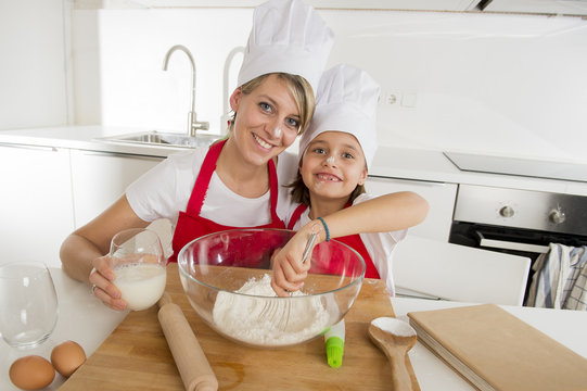 young mother and little sweet daughter in cook hat and apron cooking together baking at home kitchen