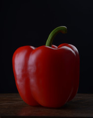 Red bell peppers on a dark wooden table on a black background.