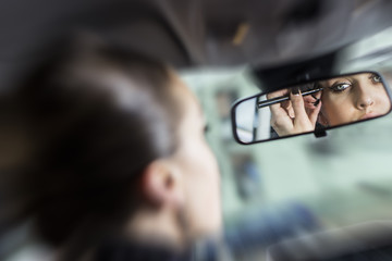 Gorgeous woman putting her mascara on while sitting in her car. Looking at her front mirror while putting makeup on. Beautiful woman driver.