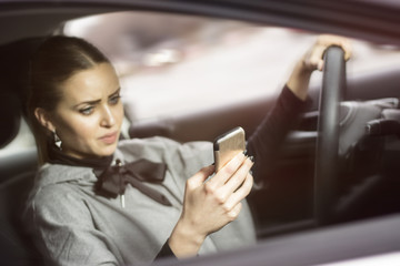 Woman texting while driving. Beautiful blonde woman driving her automobile and texting on her smartphone.