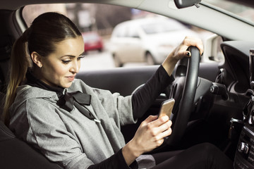 Woman texting while driving. Beautiful blonde woman driving her automobile and texting on her smartphone.