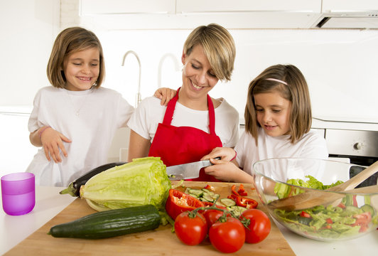young mother in cook apron and sweet beautiful twin daughters cooking preparing together salad