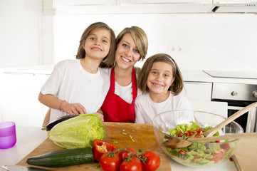 young mother in cook apron and sweet beautiful twin daughters cooking preparing together salad