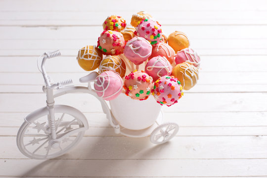 Bright cake pops  in decorative bicycle on white wooden backgrou