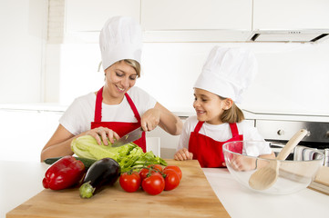 mother and little daughter cooking together with hat apron preparing salad at home kitchen