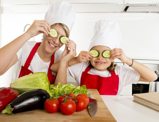 mother and little daughter cooking together playing with cucumber slices on the eyes