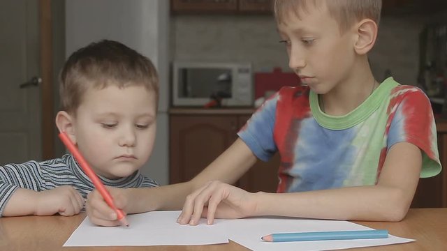 the older boy shows and says how to draw a crayon and teaches the younger boy