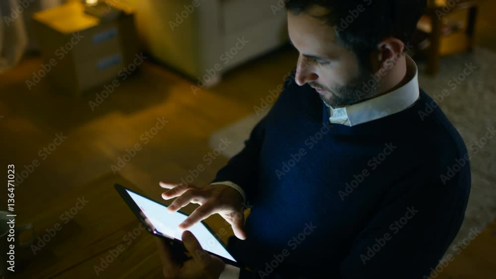 Poster respectable middle aged man sitting at his desk using tablet computer. he's at home alone. in the ba