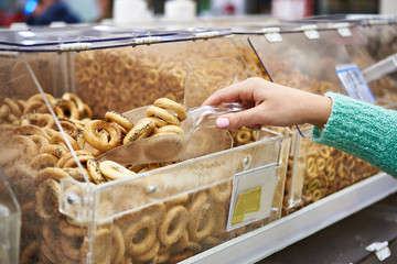 Woman buyer in shop buys bagels with poppy using scoop