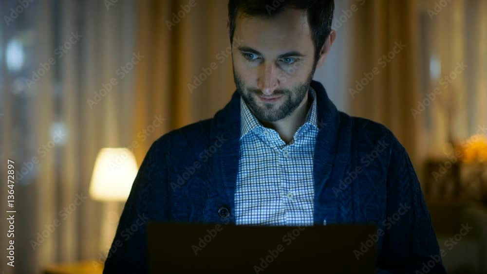 Poster portrait of a man at home working on a computer. screen illuminates him. his apartment is done in wa