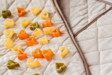 Different colored Italian pasta in hearts shape on the kitchen textiles. Food background. Assortment of colorful macaroni