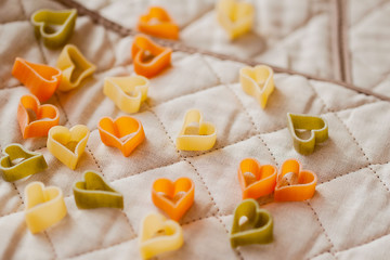 Different colored Italian pasta in hearts shape on the kitchen textiles. Food background. Close-up colorful macaroni.