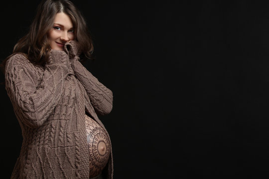 Pregnant woman posing with flower ornament on her belly, on black background.