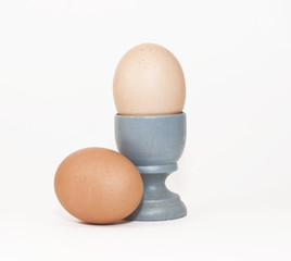 Two brown eggs and a blue wooden eggcup against a white background