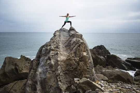 Woman practicing worrier 2 pose on rocks by sea