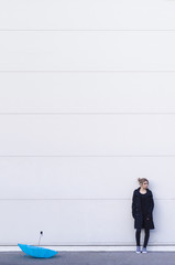 Young woman with umbrella standing by white wall