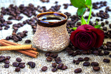cup of black coffee with coffee beans and cinnamon, red rose on sacking