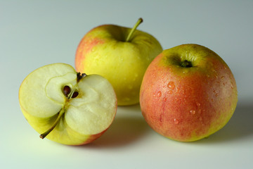 Three ripe apples, covered with drops of water, on a white background - one apple cut in half